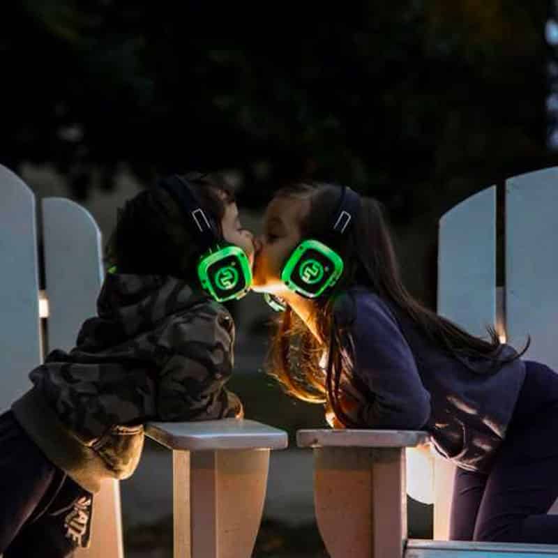 kids-silentexperience Zwei Mädchen mit Kopfhörern mit grünen LEDs umarmen sich am Abend