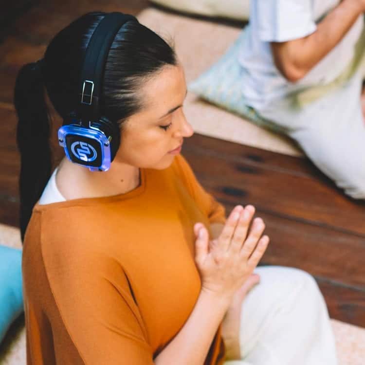 newyogi Frau meditiert mit kabellosen Kopfhörern bei einer Silent-Yoga-Stunde