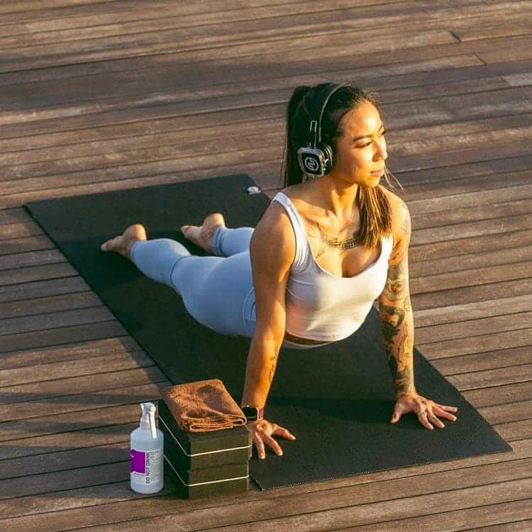 sun-yoga Yoga-Kobra-Haltung auf einer Holzplattform mit kabellosen Kopfhörern