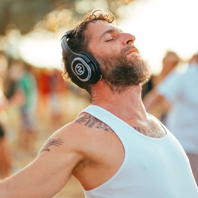 yoga-kalemana Mann atmet mit geschlossenen Augen und kabellosen Kopfhörern beim Yoga